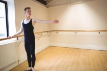Jovem bailarino alongamento no barre enquanto pratica dança de balé em estúdio — Fotografia de Stock
