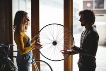 Mechanics interacting while examining a bicycle wheel in workshop — Stock Photo