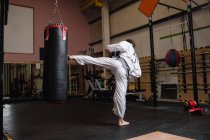 Vista posteriore dell'uomo che pratica karate con sacco da boxe in palestra — Foto stock
