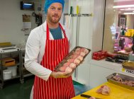 Carnicero sosteniendo una bandeja de pollo y filetes en la carnicería - foto de stock