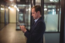 Empresário digitando uma mensagem no celular no corredor do escritório — Fotografia de Stock