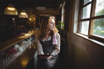 Thoughtful waitress sitting at counter and looking through window in workshop — Stock Photo