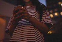 Mujer joven usando el teléfono móvil en la ciudad por la noche - foto de stock