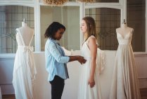 Femme essayant robe de mariée dans un studio avec l'aide du créateur de mode — Photo de stock