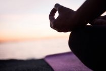 Cropped image of woman sitting in lotus position with mudra gesture on beach at dusk — Stock Photo