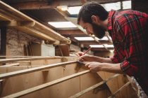 Mann misst Holzplanke in Bootswerft — Stockfoto
