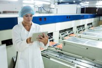 Женщины-сотрудники используют цифровые планшеты рядом с производственной линией на яйцефабрике — стоковое фото