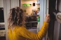 Mujer buscando comida en nevera en la cocina en casa - foto de stock