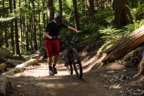 Чоловічий велосипедист, що йде з гірським велосипедом у лісі — стокове фото