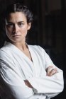Портрет женщины в кимоно карате, стоящей со скрещенными руками в фитнес-студии и смотрящей в камеру — стоковое фото