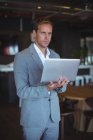 Businessman standing with a laptop in cafe — Stock Photo