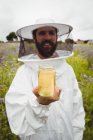Apicoltore in possesso di bottiglia di miele in campo — Foto stock