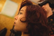 Стиліст волосся висушує волосся жінки в професійному салоні — стокове фото