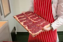 Sección media del carnicero sosteniendo una bandeja de filetes en la carnicería - foto de stock