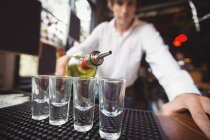 Крупный план бармена, наливающего текилу в рюмки на барной стойке в баре — стоковое фото