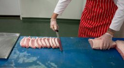Mid section of butcher slicing meat at butchers shop — Stock Photo