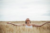 Femme debout avec les bras tendus dans le champ — Photo de stock