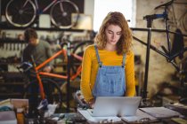 Mechanic using laptop at counter in bicycle shop — Stock Photo