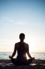 Vue arrière de la femme pratiquant le yoga sur la plage pendant le coucher du soleil — Photo de stock
