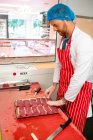 Macellaio che organizza bistecche in vassoio in macelleria — Foto stock