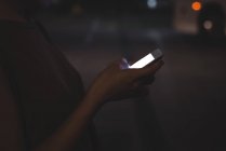 Sección media de la mujer usando el teléfono móvil en la calle por la noche - foto de stock
