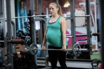 Pregnant woman working out with barbell in gym — Stock Photo