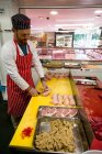 Carnicero picando pollo en el mostrador de trabajo en la carnicería - foto de stock