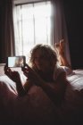 Beautiful woman taking photo on mobile phone in bedroom at home — Stock Photo