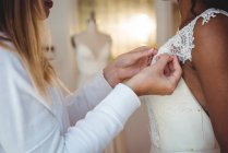 Mulher tentando em vestido de noiva em um estúdio com a ajuda do designer de moda — Fotografia de Stock