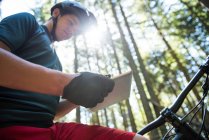 Мужчина-велосипедист, использующий цифровые планшеты в лесу при солнечном свете — стоковое фото