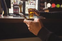 Man using mobile phone with glass of beer in hand at bar — Stock Photo