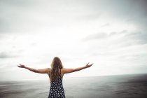 Rear view woman standing with arms outstretched on cliff over sea — Stock Photo