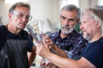 Glassblowers interacting while examining glass vase in glassblowing factory — Stock Photo
