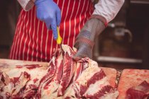 Parte média do açougueiro cortando carne vermelha no talho — Fotografia de Stock
