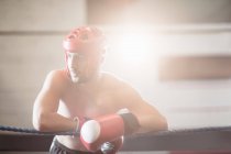 Boxer in protective boxing helmet leaning on ropes of boxing ring at fitness studio — Stock Photo