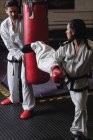 Combattenti maschi e femmine che praticano karate con sacco da boxe in studio — Foto stock
