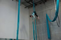 Gimnasta femenina ejercitándose sobre una cuerda de tela azul en un gimnasio - foto de stock