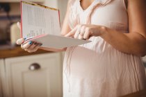 Imagem recortada da mulher grávida lendo livro na cozinha em casa — Fotografia de Stock