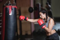 Side view of Female boxer practicing boxing with punching bag in fitness studio — Stock Photo