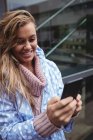 Усміхнена жінка у вітряній вітрильниці, використовуючи смартфон на вулиці — стокове фото