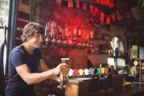Бар тендер, предлагающий бокал пива клиенту на стойке бара — стоковое фото