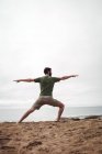 Rear view of man performing stretching exercise on beach — Stock Photo