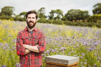 Портрет пчеловода, стоящего с руками, скрещенными на цветочном поле — стоковое фото