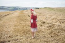 Vista trasera de mujer rubia despreocupada en vestido rojo caminando en el campo - foto de stock