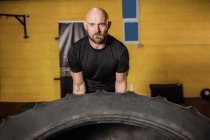 Handsome sportsman lifting heavy tire in gym and looking at camera — Stock Photo