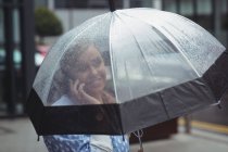 Femme tenant parapluie tout en parlant par smartphone pendant la saison des pluies — Photo de stock