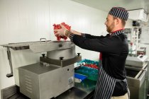Carnicero poniendo carne en la máquina picadora en la carnicería - foto de stock