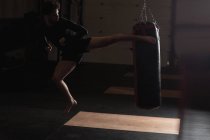 Боксер, практикуючи бокс з боксерської груші в темних фітнес-студія — стокове фото