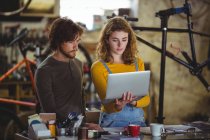 Mechanics using laptop at counter in bicycle shop — Stock Photo