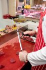 Mid section of butcher sharpening knife in butchers shop — Stock Photo